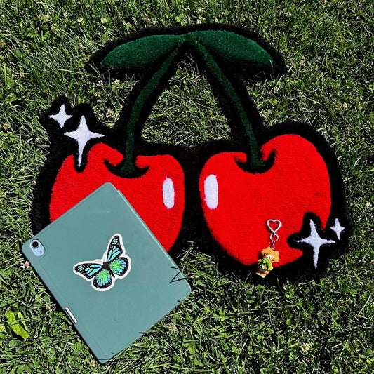 Two red cherries with black stems on a grassy background